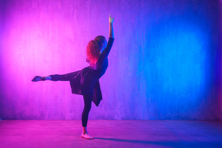 Modern dance girl dancer dancing in neon light doing gymnastic exercises in studio, copy space.の写真素材