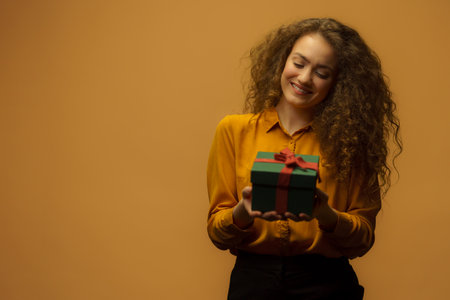 Portrait of happy young woman holding gift box, orange background.の写真素材