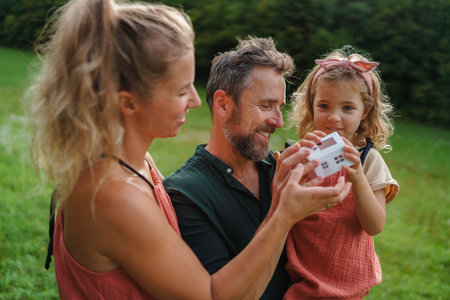 Little girl with her parents holding paper model of house with solar panels.Alternative energy, saving resources and sustainable lifestyle concept.の写真素材