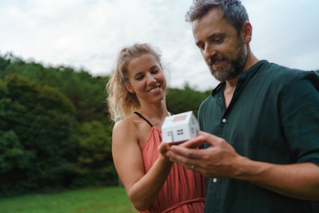 Close up of happy couple holding paper model of house with solar panels, looking and dreaming about future. Alternative energy, saving resources and sustainable lifestyle concept.の写真素材