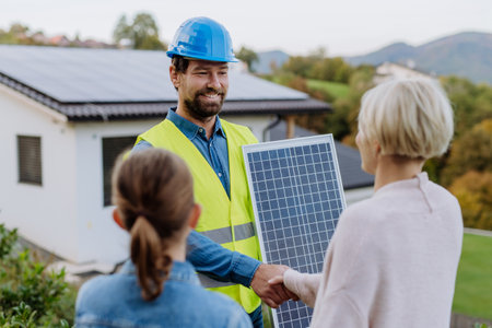 Smiling handyman, photovoltaics panels installer shaking hand with family owner of house.の写真素材