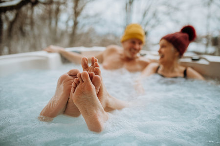 Senior couple in kintted cap enjoying together outdoor bathtub at their terrace during cold winter day.の写真素材