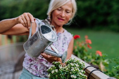Senior woman watering her flowers on terrace and enjoying view at forest.の写真素材