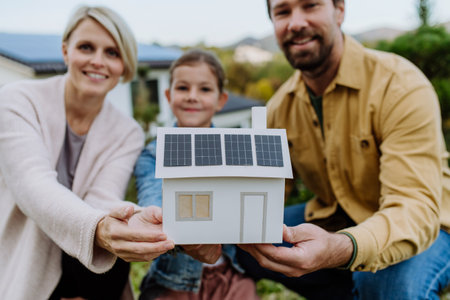 Happy family holding paper model of house with solar panels.Alternative energy, saving resources and sustainable lifestyle concept.の写真素材