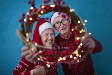 Portrait of happy senior couple with Santa Claus hats in studio, looking trough Christmas wreath.の写真素材