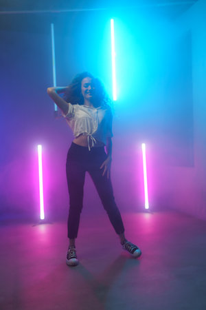 Modern dance girl dancer dancing in neon light doing gymnastic exercises in studio, copy space.