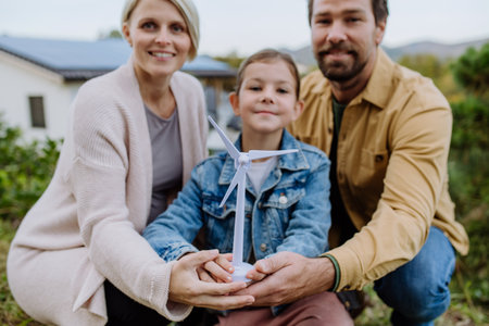 Happy family holding plastic model of wind turbine. Alternative energy, saving resources and sustainable lifestyle concept.の写真素材