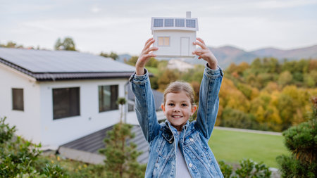 Happy little girl holding paper model of house with solar panels.Alternative energy, saving resources and sustainable lifestyle concept.の写真素材