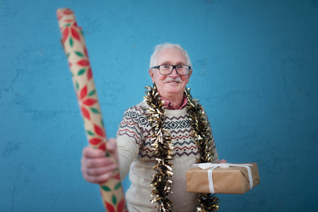 Portrait of happy senior man holding Christmas gift and wrapping paper studio shooting.の写真素材