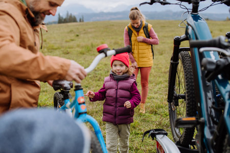 Young family with little children preparing for bicycle ride in nature, putting off bicycles from...