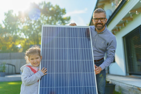 Father with his little daughter near their house with solar panels. Alternative energy, saving resources and sustainable lifestyle concept.の写真素材