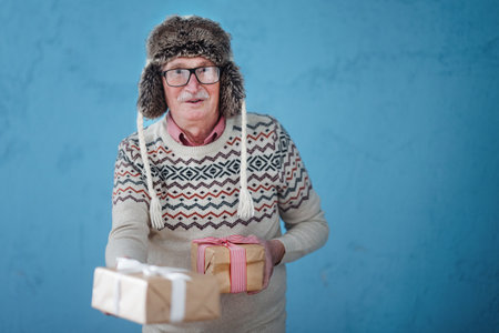 Portrait of happy senior man in warm Chrstimas cap holding gifts.
