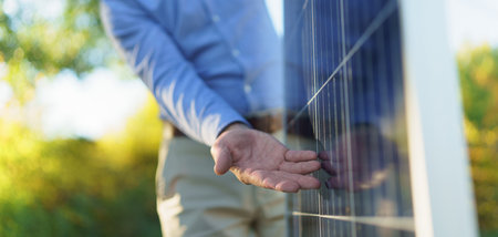 Mid section of businessman holding solar panel, standing outdoor at garden.の写真素材