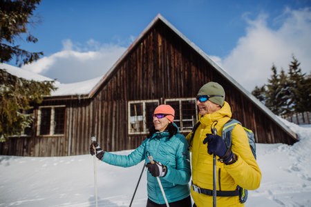 Senior couple having break during skying, next forest cottage.の写真素材