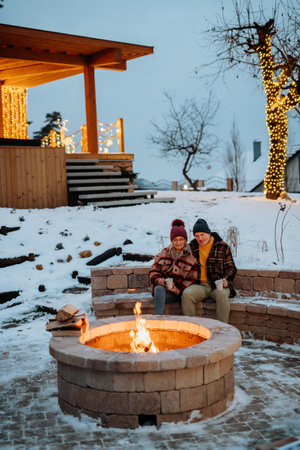 Senior couple sitting and heating together at outdoor fireplace in winter evening.の写真素材