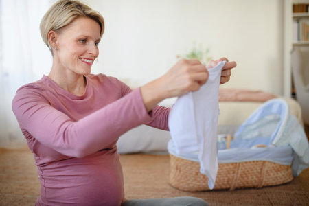 Happy pregnant woman looking at little clothes for her baby.