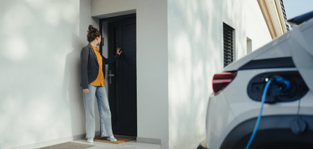 Young woman preparing to work while her electric car charging in home, sustainable and economic transportation concept.の写真素材