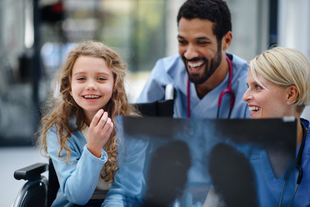 Young multiracial doctor with his colleague showing x-ray image of lungs to little girl on wheelchair.の写真素材