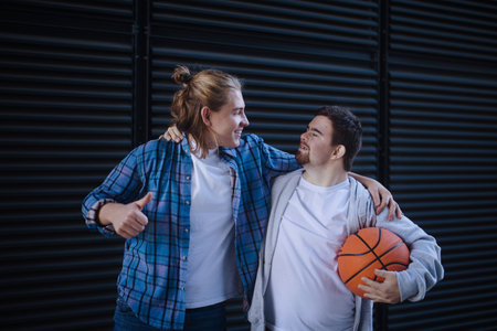Man with down syndrome playing basketball outdoor with his friend. Concept of friendship and integration people with disability into society.の写真素材