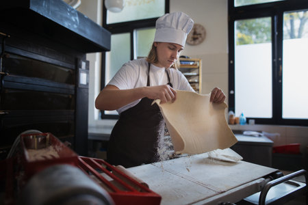 Young baker with chef cap preparing pastries in bakery.の写真素材