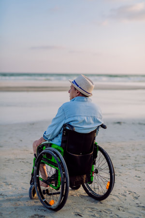Rear view of man sitting on wheelchair and enjoying view at sea.の写真素材
