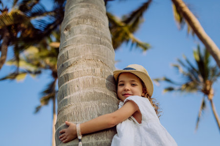 Happy little girl hugging palm tree during tropical vacation.