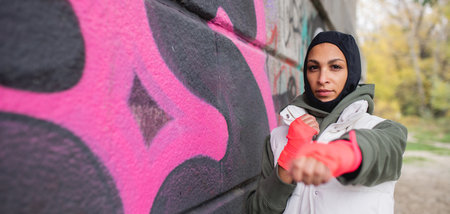 Portrait of young muslim woman with sports gloves, standing in front of graffiti.の写真素材