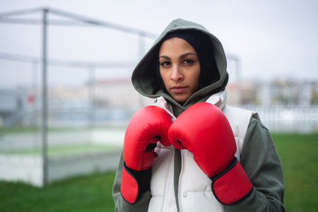 Portrait of young muslim woman with boxing gloves standing outdoor.の写真素材