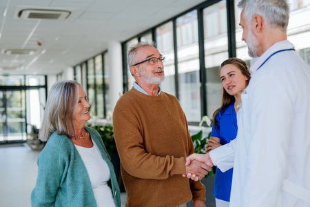 Mature doctor and his young colleague talking with his senior patients at hospital corridor.の写真素材