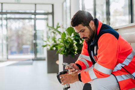 Rescuer having break, drinking coffee and scrolling his mobile phone at hospital corridor.の写真素材