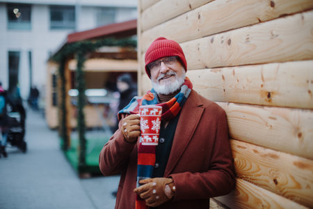 Happy senior man enjoying christmas market, drinking muled wine.