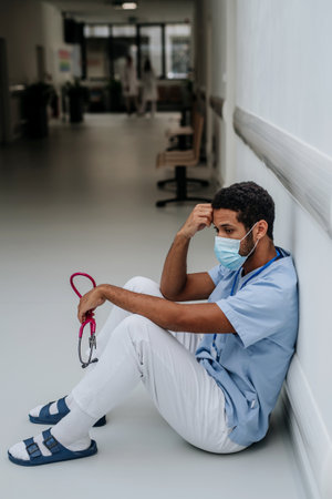 Young distressed doctor sitting at hospital corridor floor.