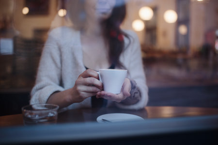 Close-up of woman holding cup of coffee, siting in a cafe.