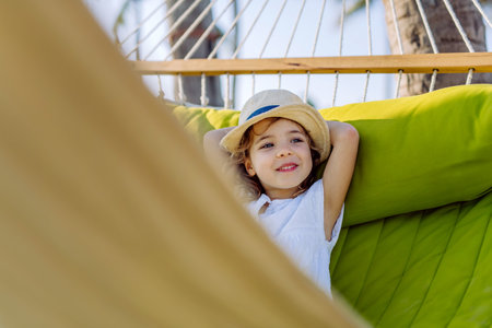 Little girl in straw hat lying in hammock and enjoying summer exotic vacation.の写真素材