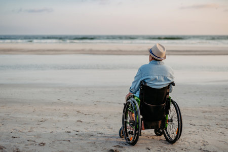 Rear view of man sitting on wheelchair and enjoying view at sea.の写真素材