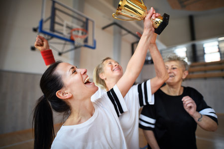 Group of young and old women, basketball team players, in gym with trophy celebrating victory.の写真素材