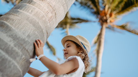 Happy little girl touching palm tree during tropical vacation.の写真素材