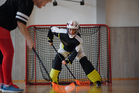 Close-up of woman floorball goalkeeper in helmet concetrating on game in gym.
