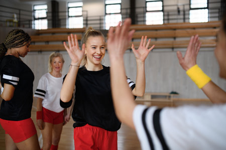 Group of young and old cheerful women, floorball team players, in gym cebrating victory.
