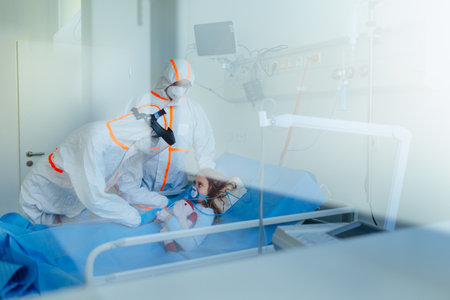 Little girl with infection disease lying in hospital room, doctors in protective coverals examining her.の写真素材