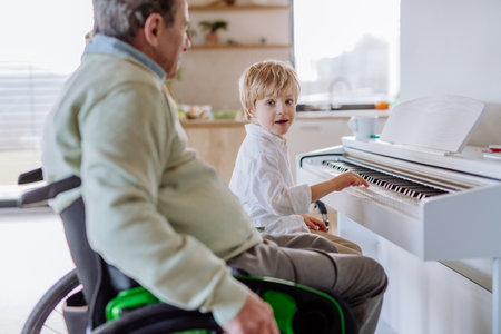 Little boy playing on the piano with his grandfather on wheelchair.の写真素材