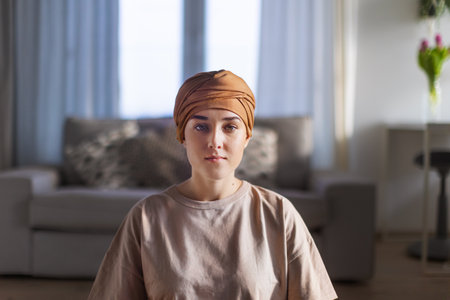 Portrait of young woman with cancer sitting in her apartment.の写真素材