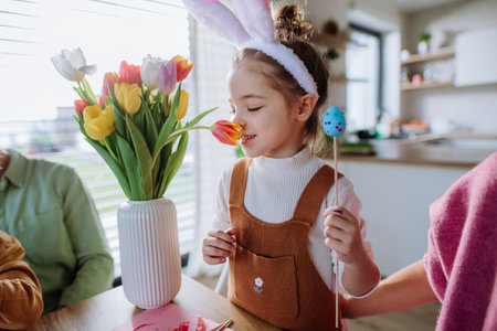 Little girl smelling bouquet of tulip flowers during decorating easter eggs with her family.の写真素材