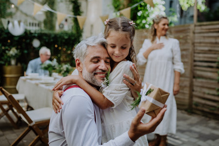 Mature father groom receiving gift from his daughter at wedding reception outside in the backyard.の写真素材