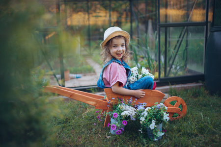 Little girl playing with wooden wheelbarrow full of flowers in their garden.の写真素材