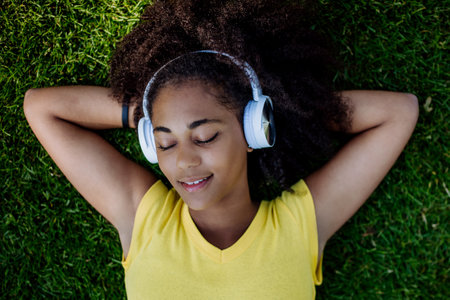 Multiracial girl lying down in grass and enjoying music in headphones, top view.の写真素材
