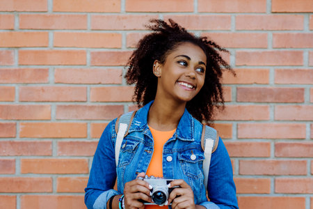 Multiracial girl standing in front of brick wall with camera, and posing.