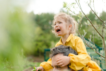 Father holding his crying little daughter and comforting her in gardenの写真素材