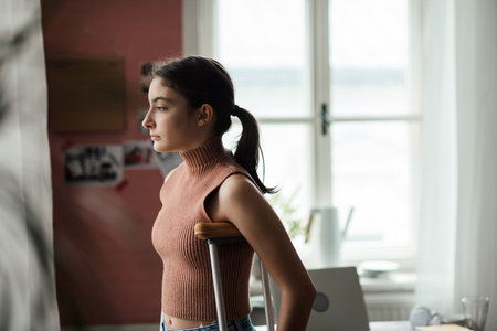 Unhappy girl with broken leg in her room looking trough windowの写真素材