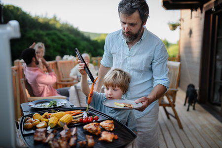 Father with little son grilling outside during family summer garden party.の写真素材